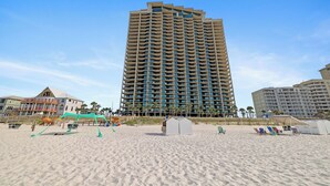 A high-rise hotel with multiple balconies, a sandy beach in the foreground, and palm trees. - Phoenix West 1108 by Liquid Life (Orange Beach)