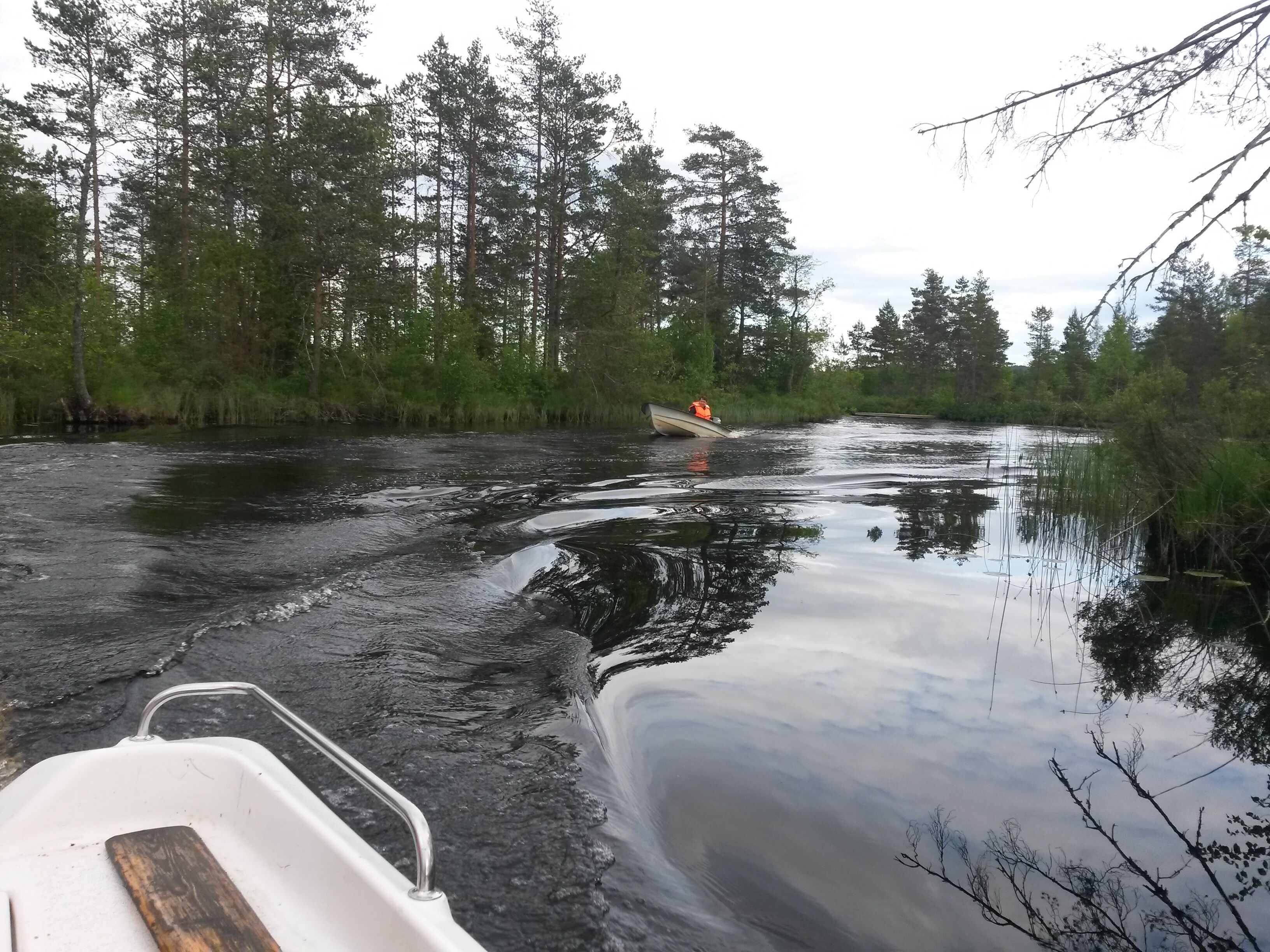 Une rivière avec un bateau et une personne portant une veste orange qui rame.