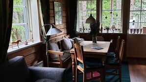 Ein gemütliches Blockhauszimmer mit einer hölzernen Bank, einem Esstisch mit Stühlen und großen Fenstern mit Blick auf den Wald.
