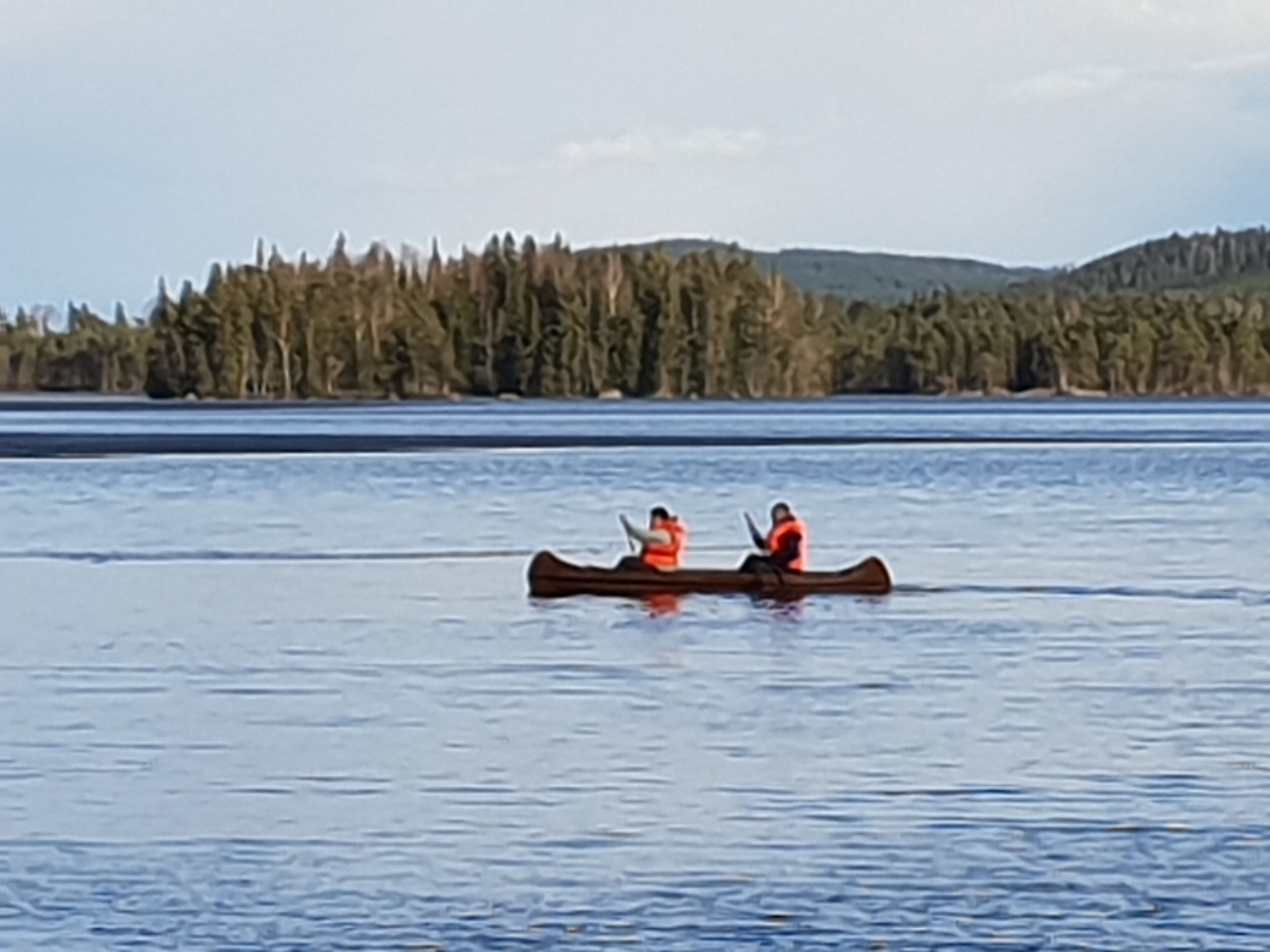 A canoe on a calm lake with a forested shoreline.