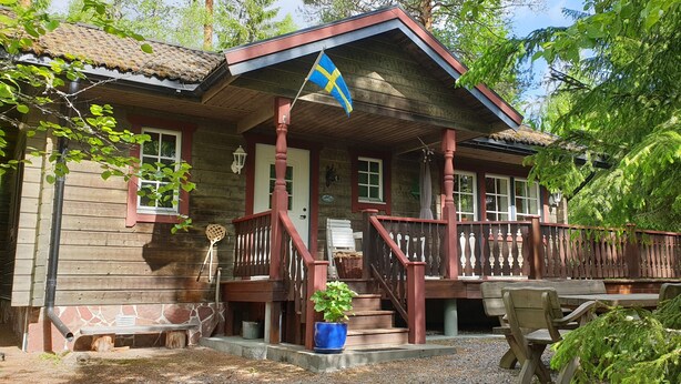 Eine Holzhütte mit Veranda, einer Flagge und Sitzmöglichkeiten im Freien.