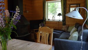Ein gemütliches Blockhaus-Interieur mit Kamin, Holzmöbeln, einer Couch und einem Tisch mit Blumenvase.
