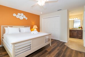 A bedroom with a bed, a ceiling fan, a nightstand with a lamp, and a bathroom with a vanity and mirror.
