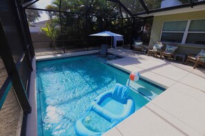 A swimming pool with a blue inflatable float, a covered seating area, and a view of a house in the background.