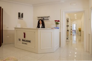 Un comptoir d’accueil portant l’inscription « Le Angioine Rooms », avec une horloge et un vase de fleurs.