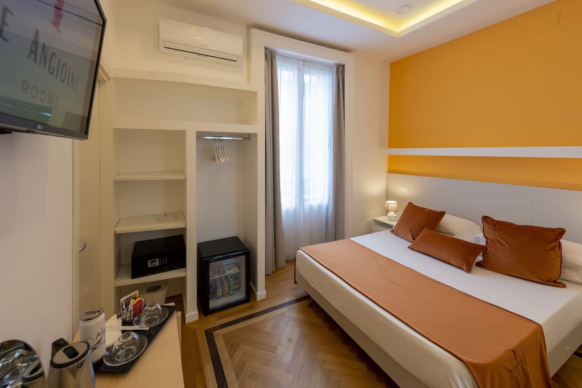 A hotel room with a bed, a television, a minibar, and a wardrobe.