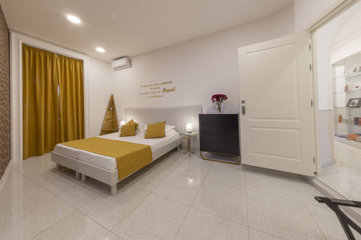 A modern hotel room with a bed, a small table, a wall-mounted TV, and a door leading to a bathroom.