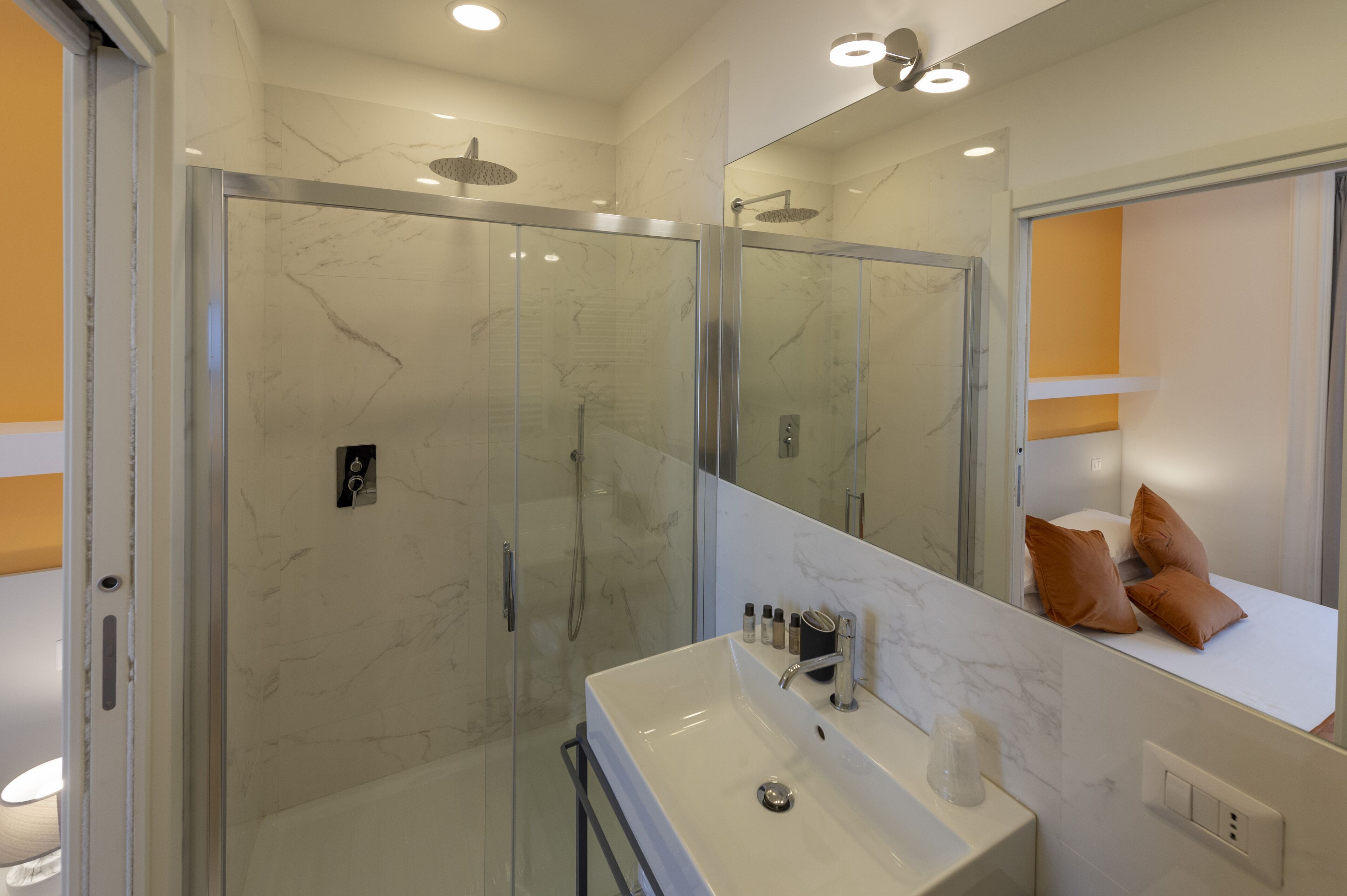 Ein modernes Badezimmer mit einer begehbaren Glasdusche, einem weißen Waschbecken und einem großen Spiegel.