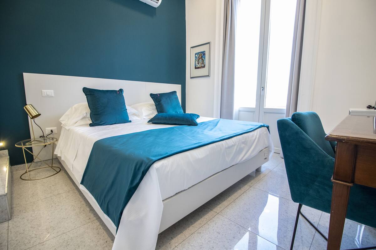 A modern hotel room with a large bed, a desk, and a chair.