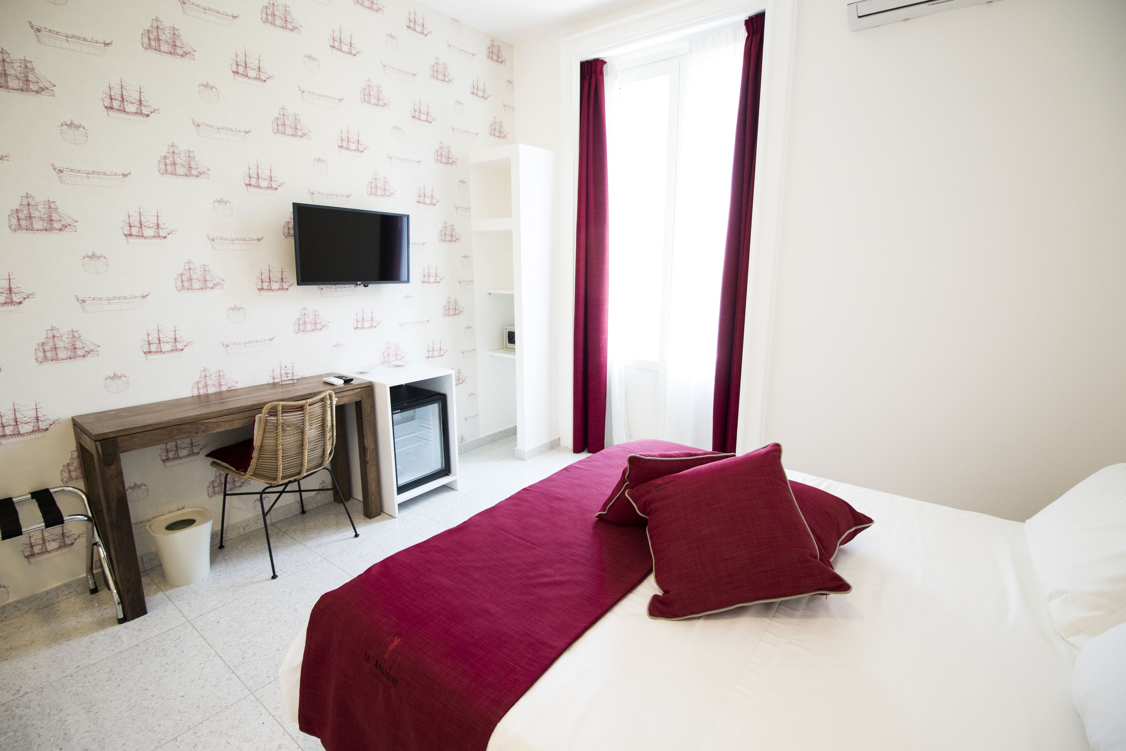 A hotel room with a bed, a desk, a chair, a television, and a window with curtains.