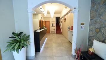 A hotel reception area with a reception desk, a staircase, and a potted plant.