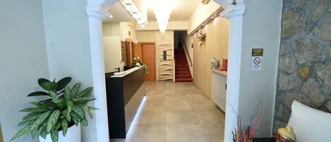 A hotel reception area with a reception desk, a staircase, and a potted plant.