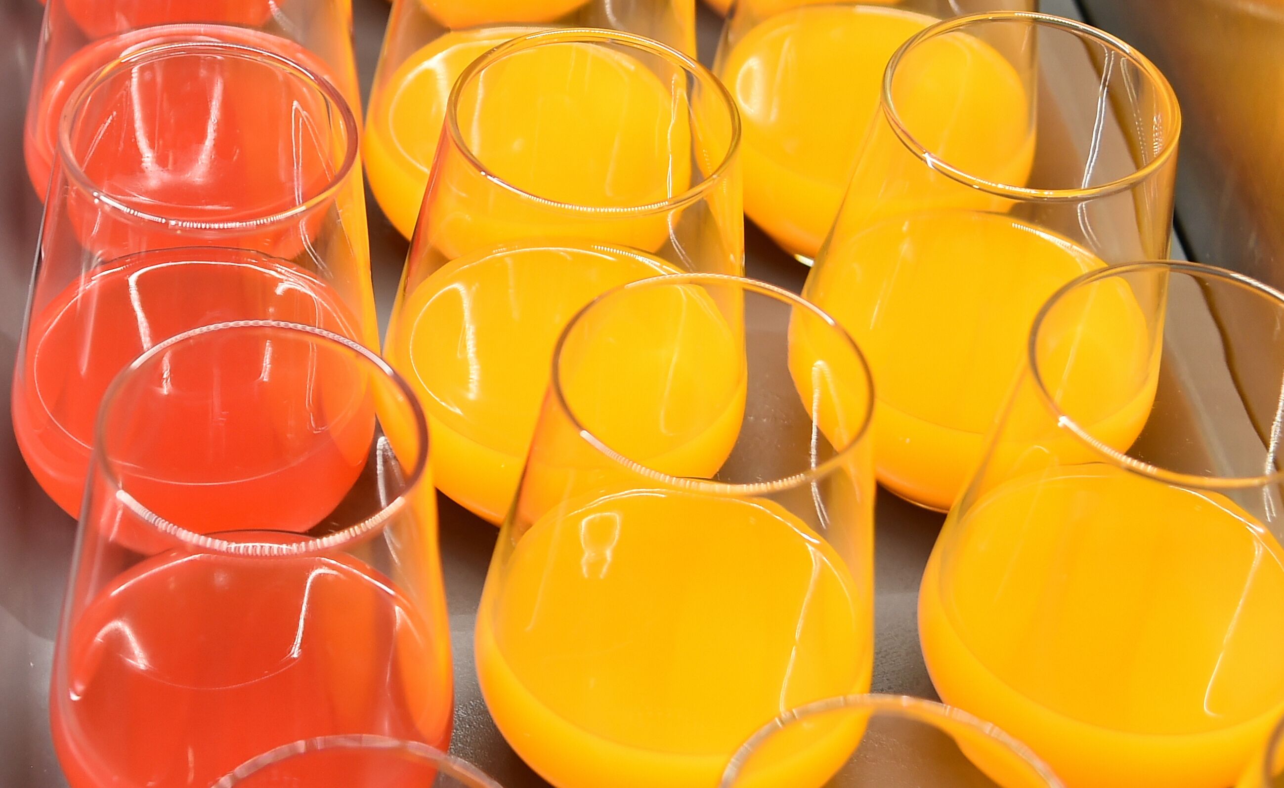 A variety of clear glasses filled with orange juice.