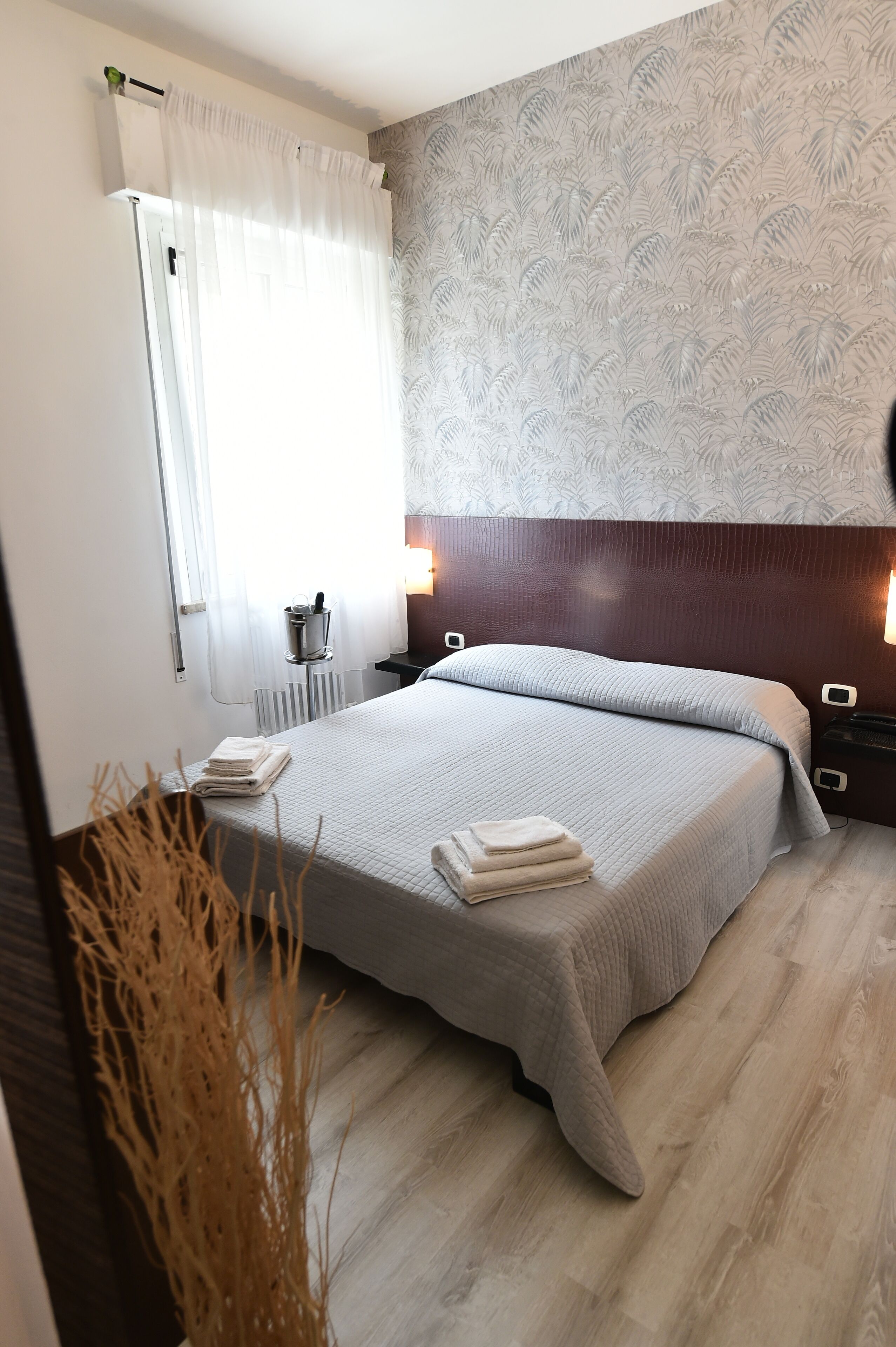 A neatly made bed with a white comforter and pillows, a bedside table with a lamp, and a radiator on the wall.