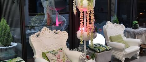 A seating area with ornate white chairs and a central decorative column with flowers and lights.