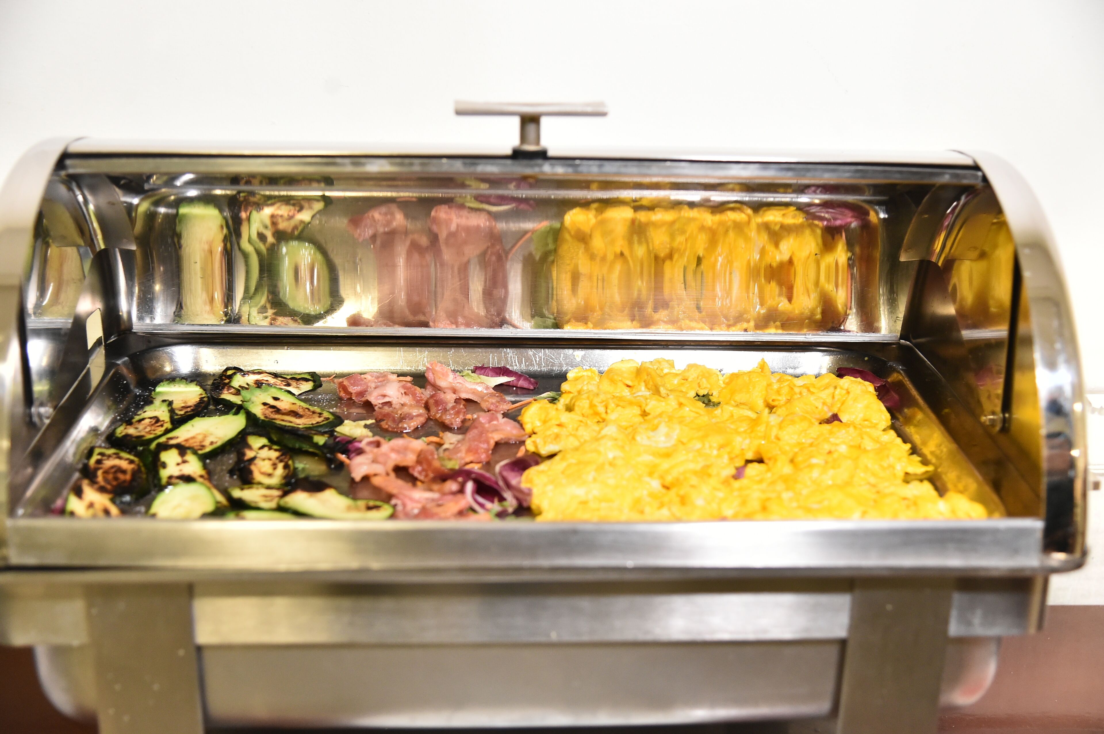 Un bufé con diversas opciones de comida, incluyendo verduras a la parrilla, carnes y arroz amarillo.