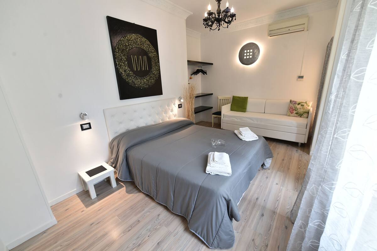 Un dormitorio moderno con una cama, mesitas de noche, un sofá blanco y una araña.
