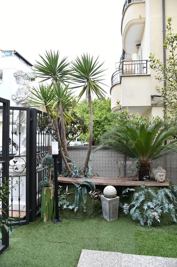 A courtyard with a statue, palm trees, and a stone bench. - Hotel Okinawa (Rimini)