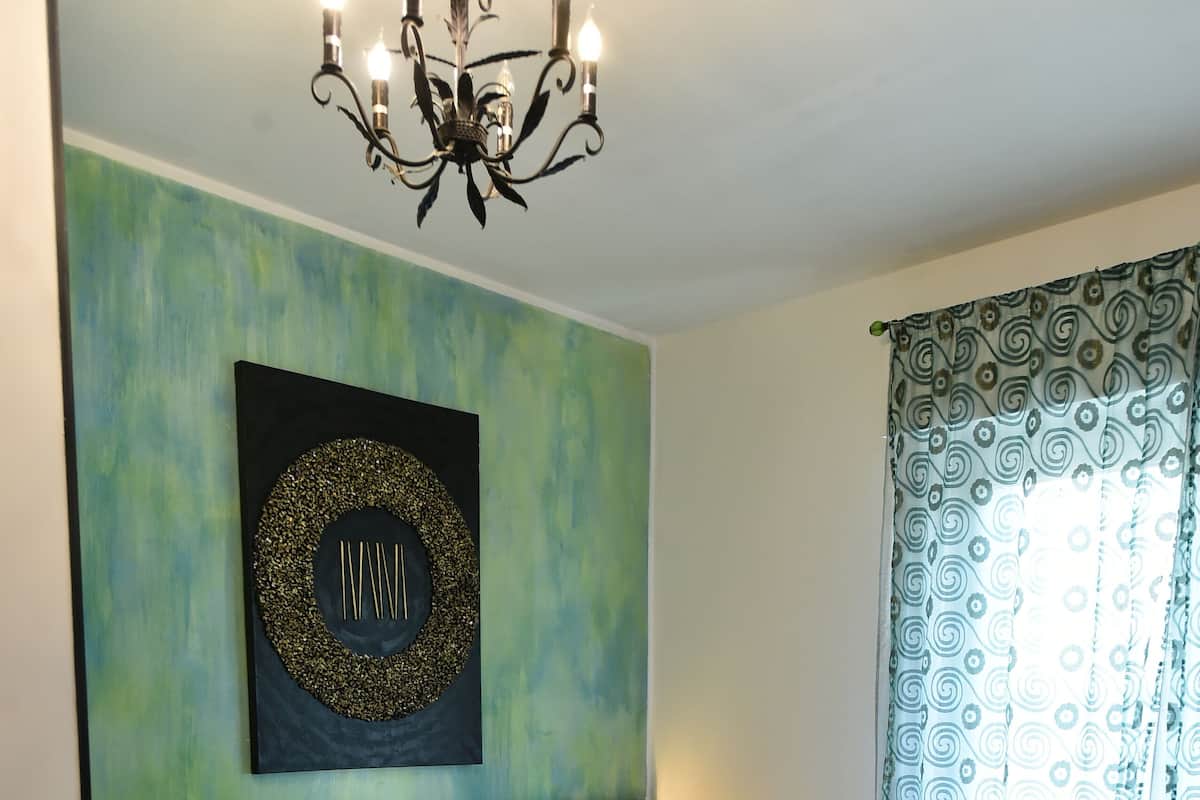 Una cama bien hecha con una colcha blanca y toallas dobladas, una obra de arte en la pared, un candelabro y cortinas estampadas.