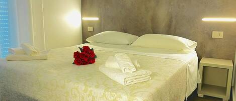 A neatly made bed with white linens, a bouquet of red roses, and a bedside table with a lamp.