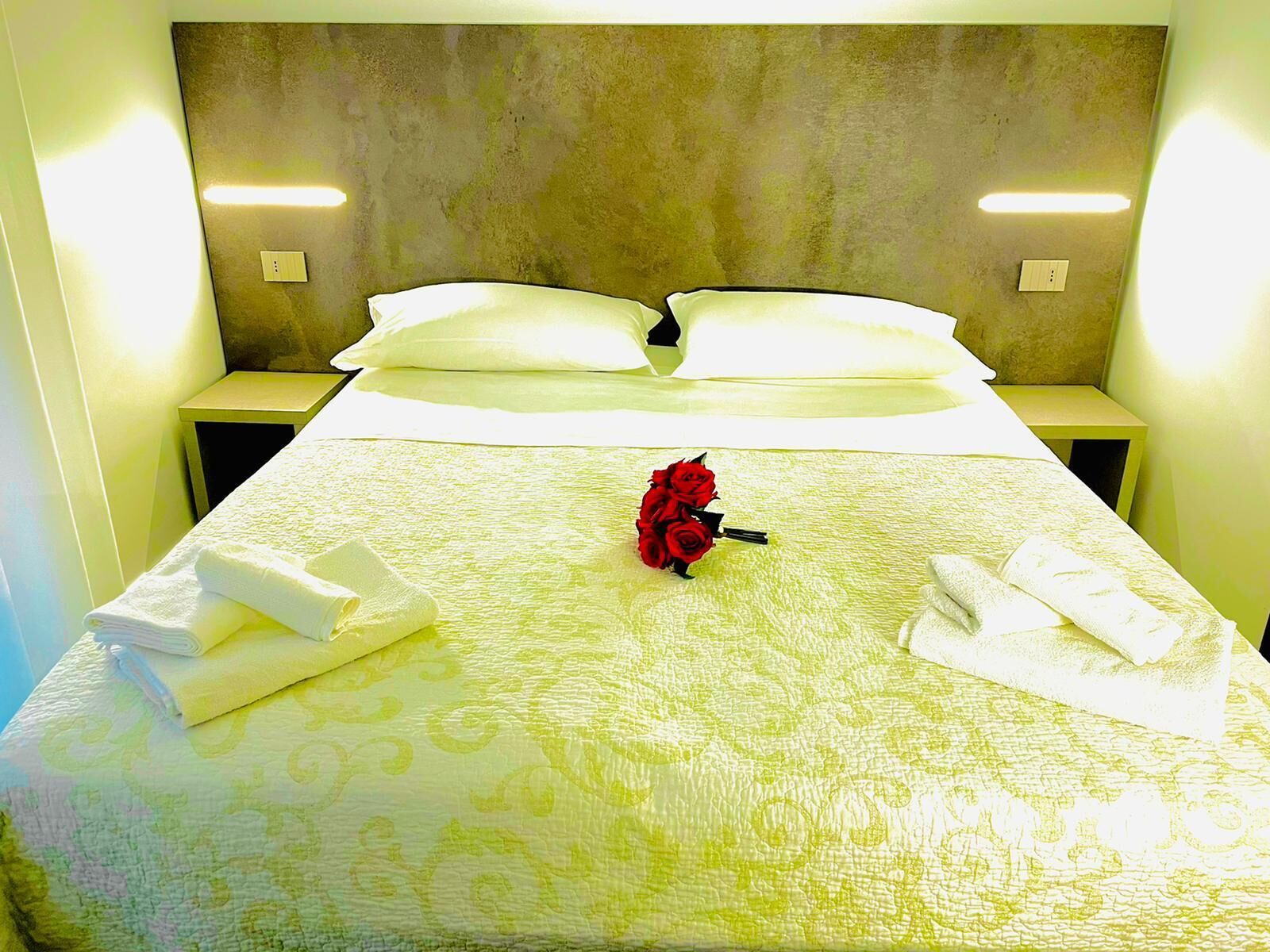 Una habitación de hotel con cama, almohadas, un ramo de rosas rojas y toallas dobladas.