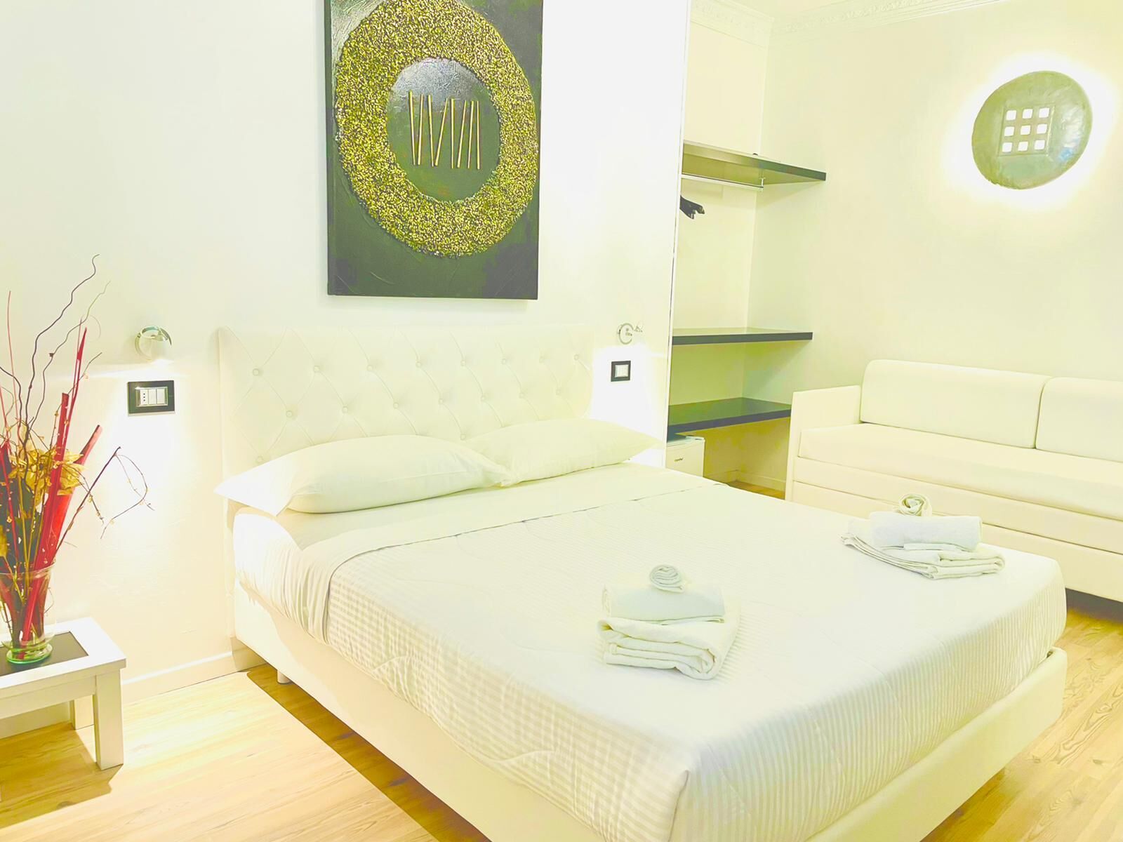 A modern bedroom with a large bed, a bedside table, a small table with a vase, and a sofa.