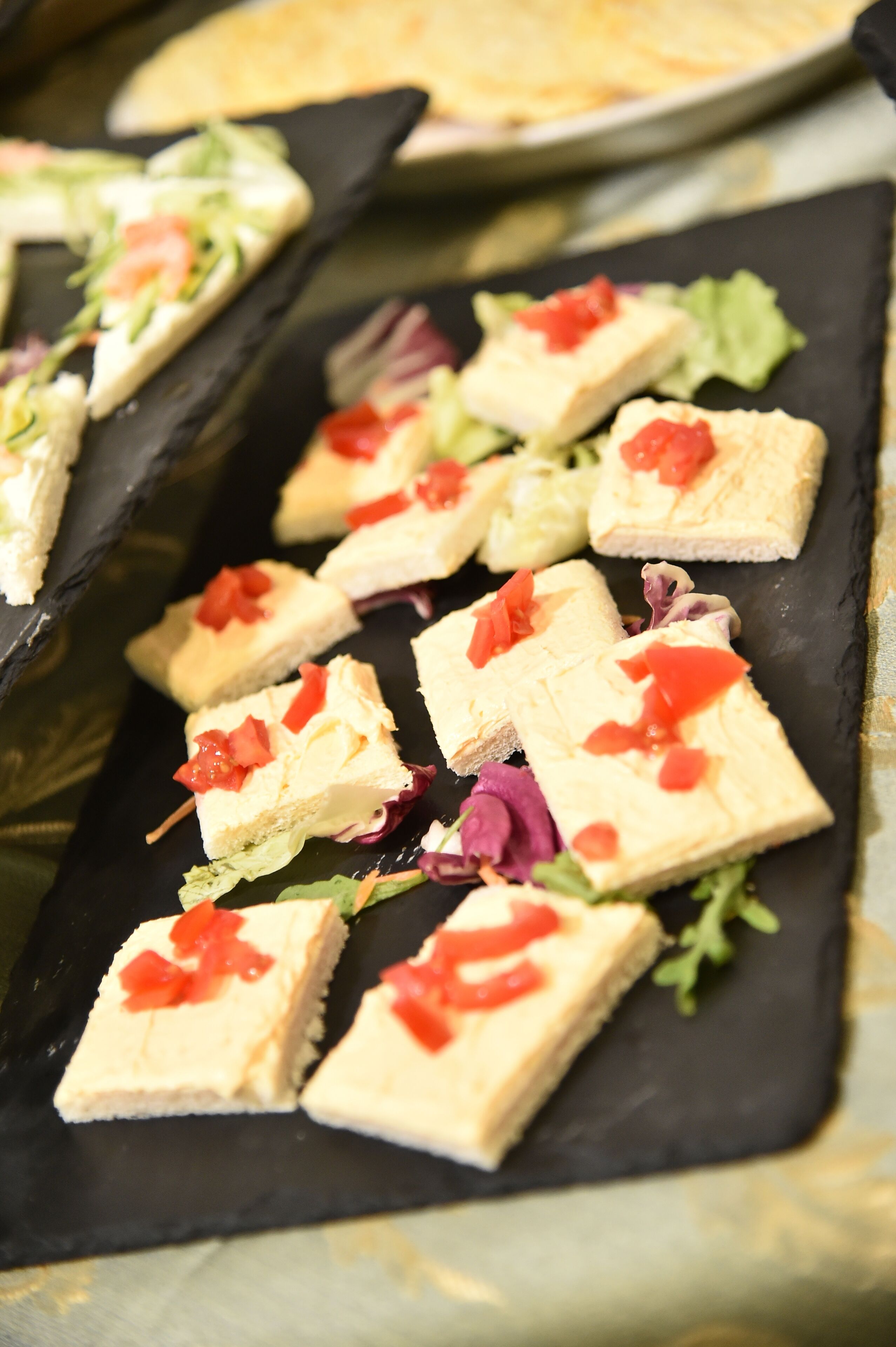 A black slate serving tray with several square pieces of food topped with red tomato pieces.