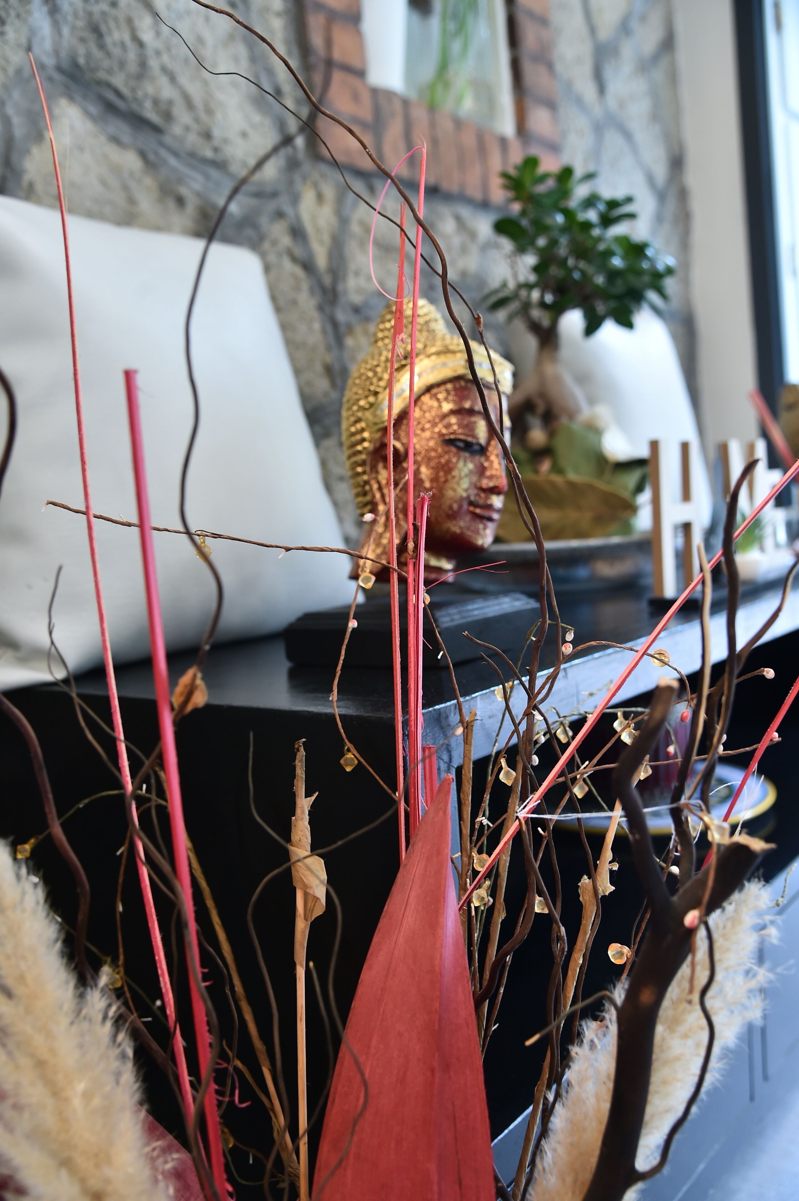 A room with a decorative Buddha statue, a potted plant, and a white pillow.