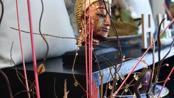 A room with a decorative Buddha statue, a potted plant, and a white pillow.