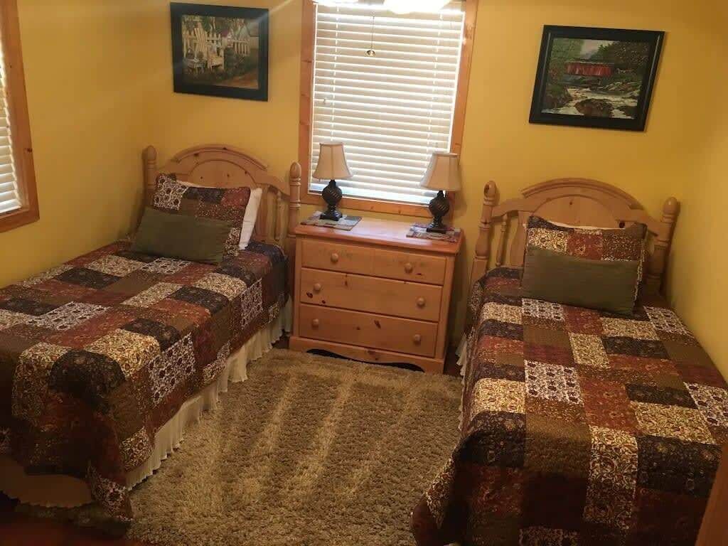 Een slaapkamer met twee enkele bedden, een houten dressoir en twee lampen.