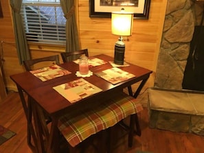 Cozy cabin dining area with a wooden table, chairs, and bench, featuring a stone fireplace and a framed picture above.