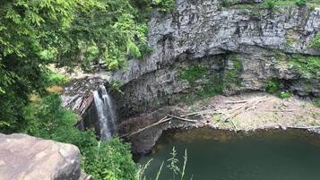 Een natuurlijke waterval die in een kalm stroompje uitmondt, omringd door rotswanden en weelderige begroeiing.