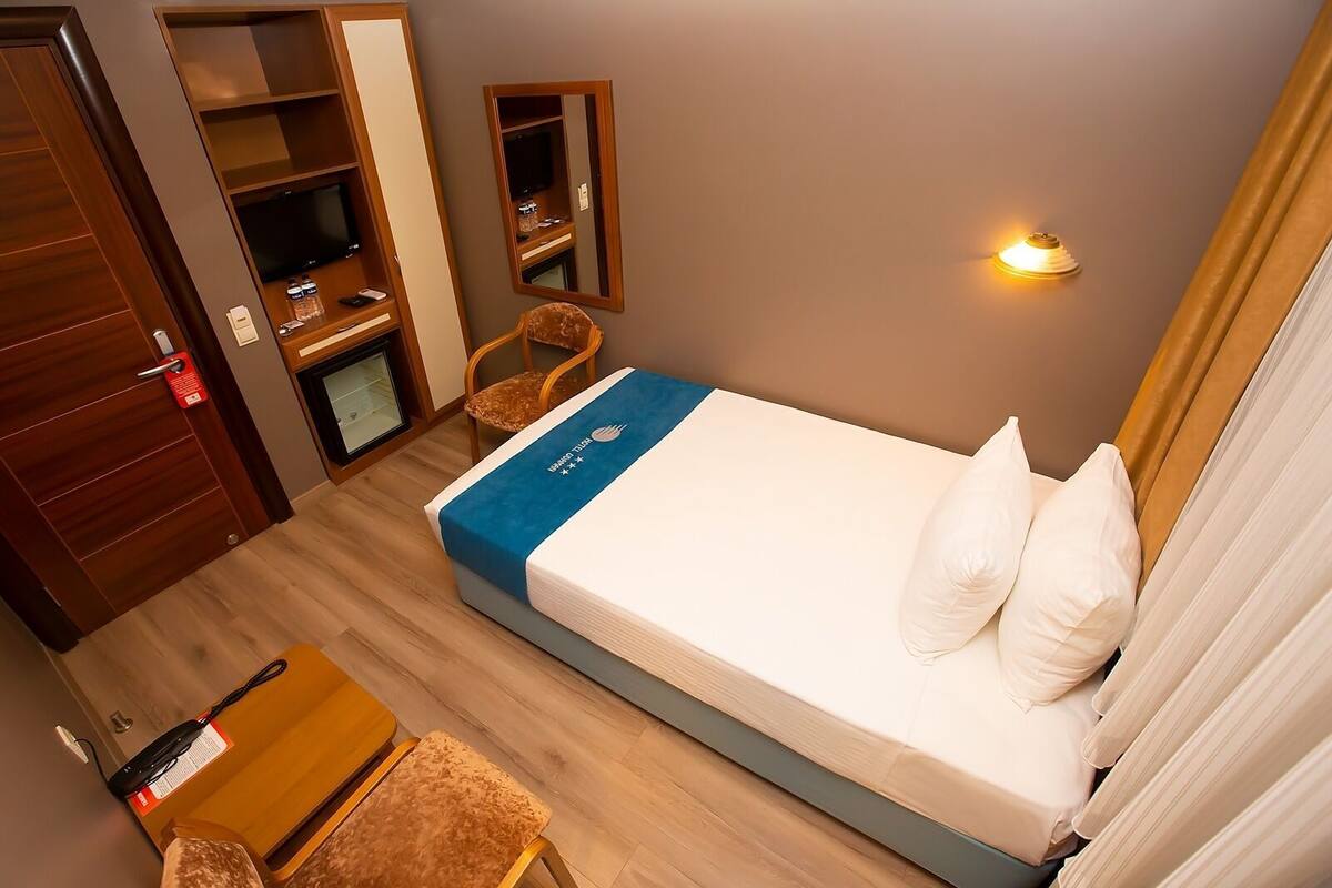 Una camera d'albergo con un letto, una scrivania, una sedia, un armadio, una televisione e una lampada a parete.