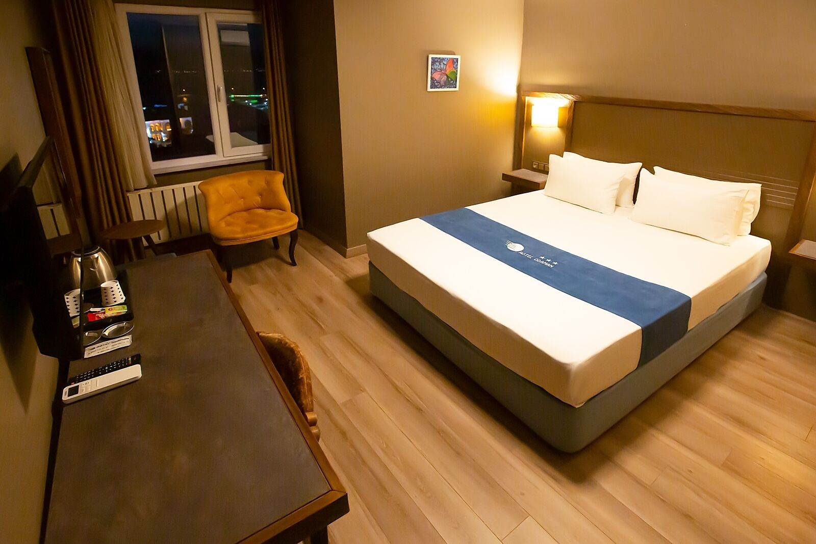 Une chambre d’hôtel avec un lit, une chaise, un bureau, une lampe et une fenêtre donnant sur la ville, avec une vue nocturne.