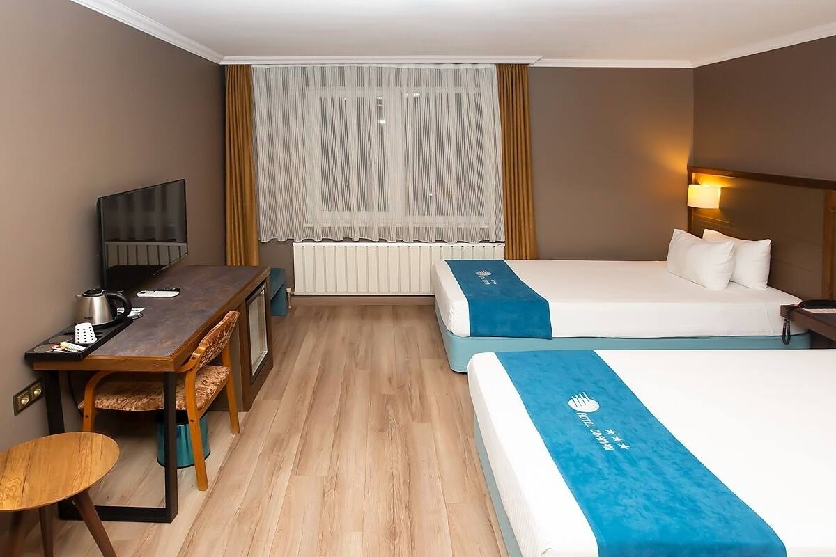 Una camera d'albergo con due letti, una scrivania, una sedia, una televisione e una finestra con tende.