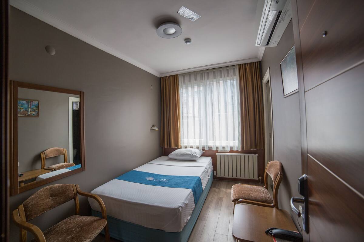 Una camera d'albergo con un letto, una scrivania, una sedia, uno specchio e una finestra con tende.
