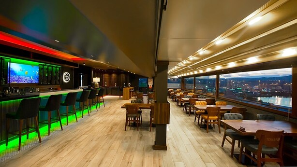 Zona de bar con un gran acuario, mostrador de madera y asientos con vistas a la ciudad.