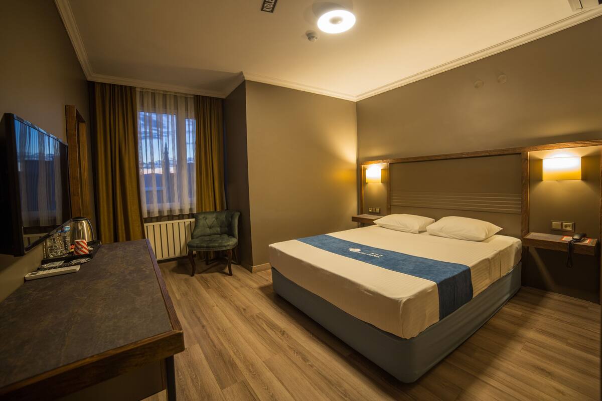Una camera d'albergo con un letto, comodini, una scrivania, una sedia e una televisione.