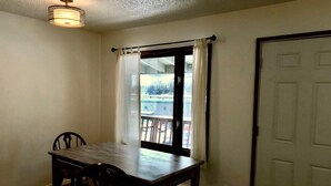 Quarto com mesa de jantar, cadeiras, janela com cortinas e porta.