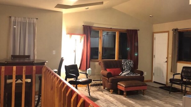 Una sala de estar con una mesa de comedor de madera, dos sillas, un sofá y una ventana con cortinas.