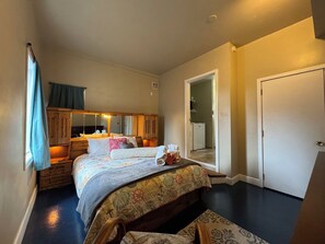 A bedroom with a bed, a dresser, a mirror, a door, and a small bathroom visible through an open door. - Sluice Box - Affordable, Convenient, and near Mendenhall Glacier- DISCOUNTS ON TOURS! (Juneau)