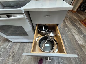 A kitchen with a white stove, a drawer with pots and pans, and a wooden floor. - Sluice Box - Affordable, Convenient, and near Mendenhall Glacier- DISCOUNTS ON TOURS! (Juneau)