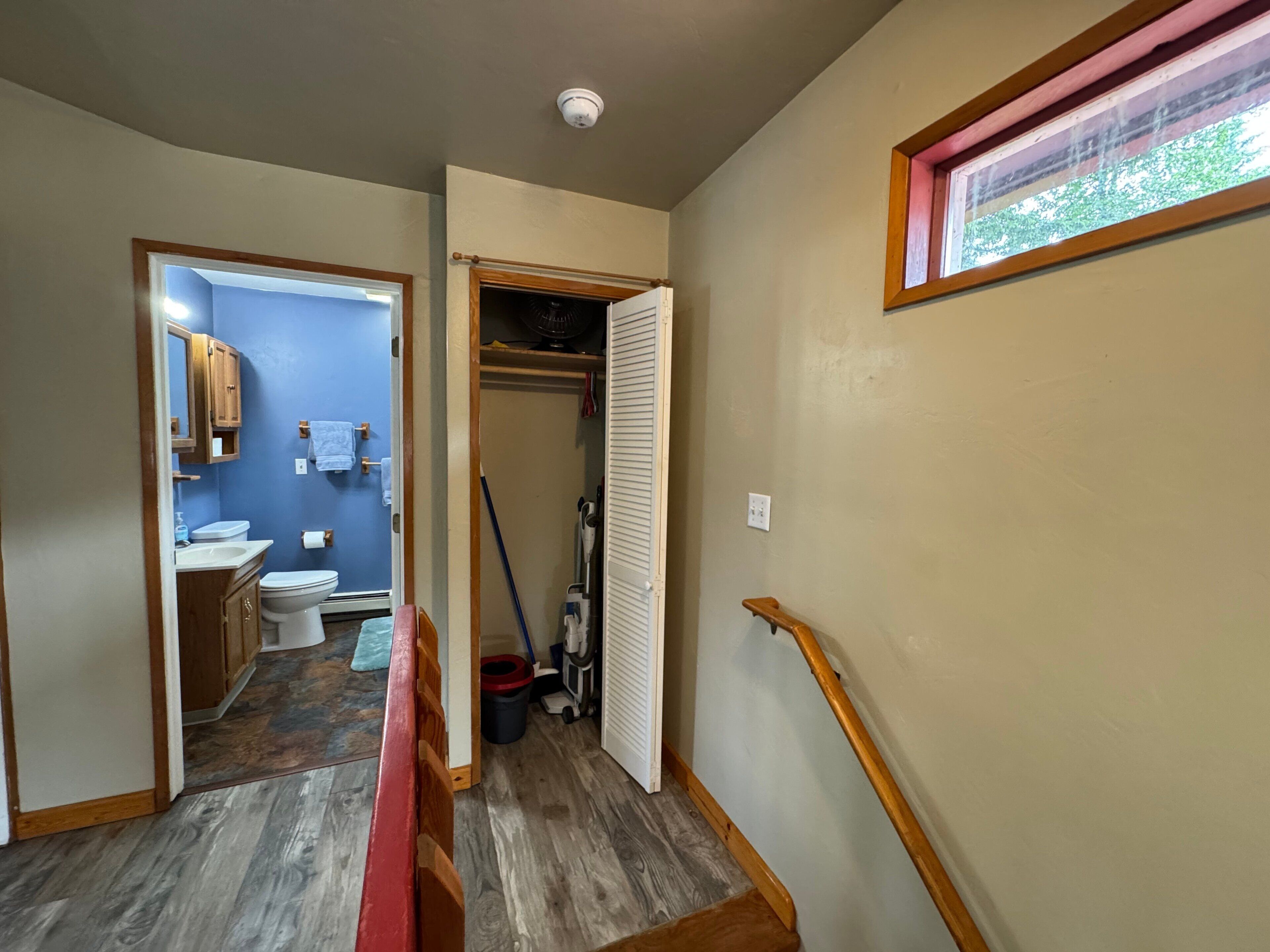 A hallway leading to a bathroom with a toilet, sink, and wooden cabinets.