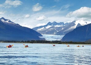 Kayakistas en un lago tranquilo, con un glaciar y montañas al fondo.
