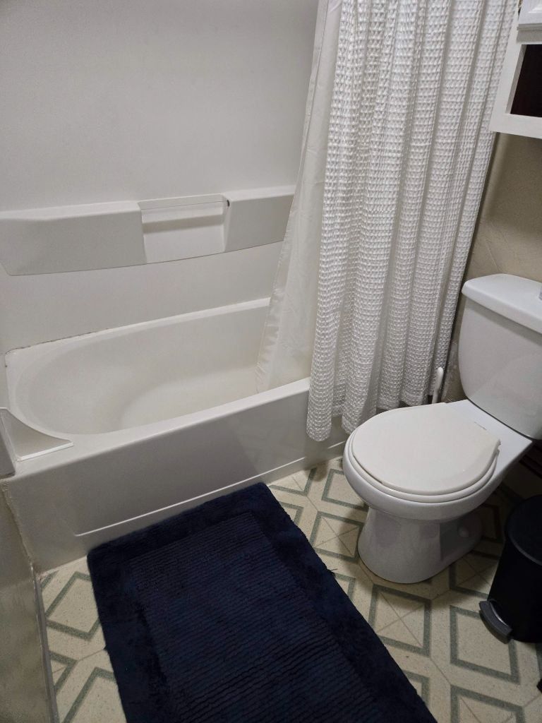 Een badkamer met een badkuip, toilet en een donkerblauwe kleed.