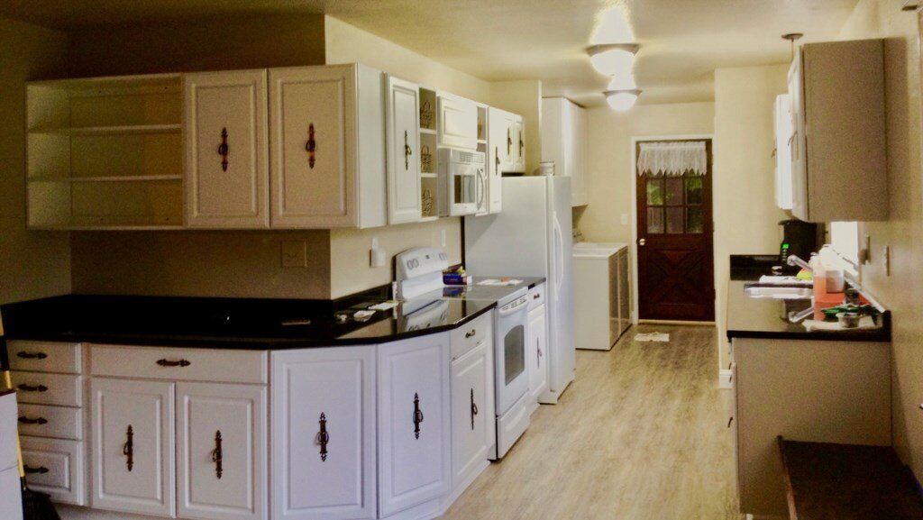 A compact kitchen with white cabinetry, a black countertop, and a microwave.