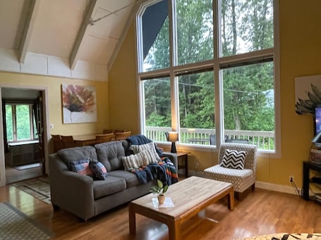 A spacious living room with a large window, a sofa, a coffee table, and a patterned armchair.