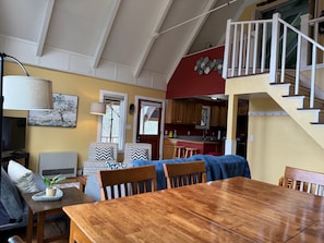 A dining area with a wooden table and chairs, a sofa, a lamp, and a staircase leading to an upper level.