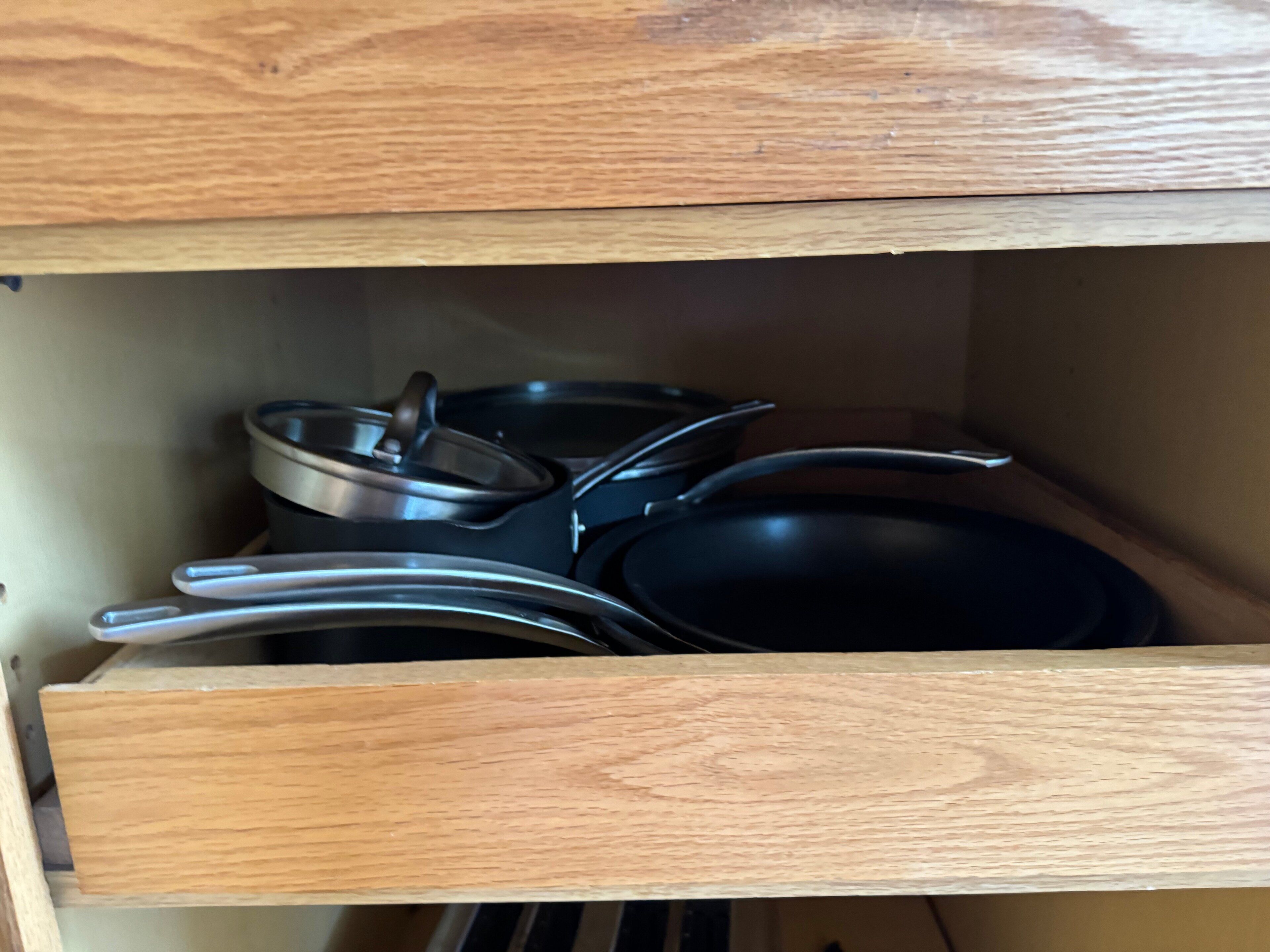 A kitchen cabinet with wooden doors and metal cookware inside.
