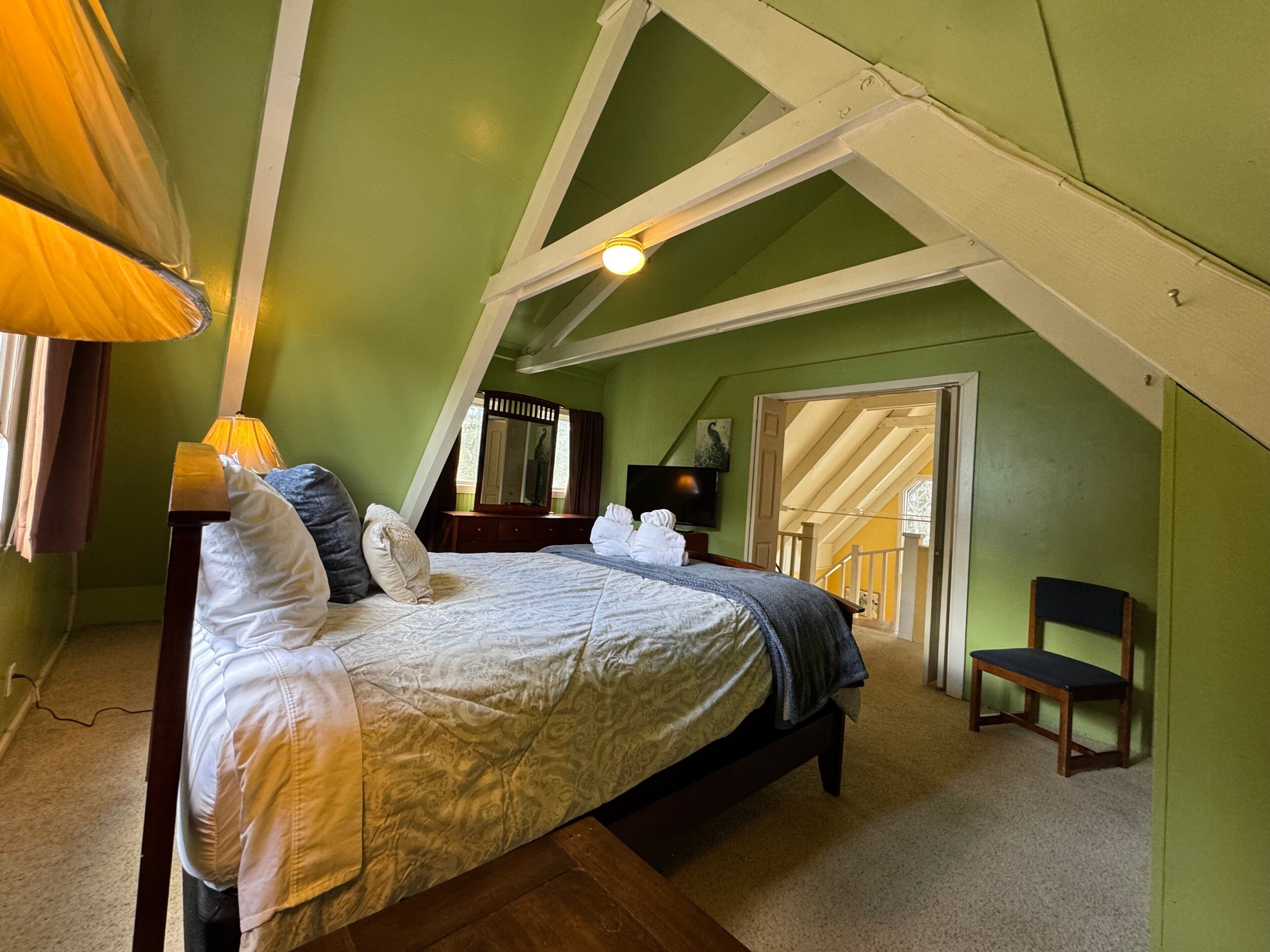 A bedroom with a bed, a chair, a TV, and a mirror.